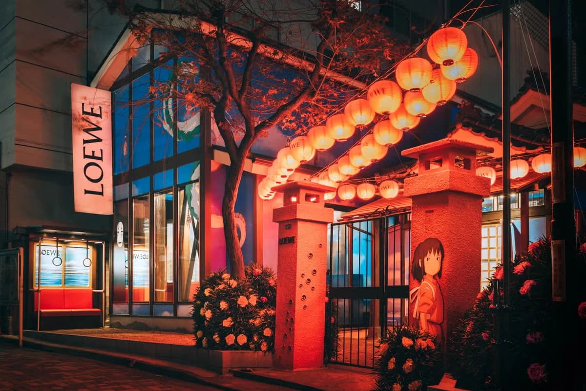 Night-time exterior of a LOEWE × Spirited Away pop-up with red lanterns, Chihiro’s silhouette and glowing signage evoking the bathhouse from the film.