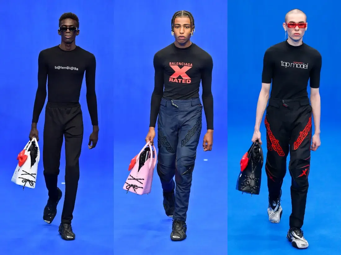 Three male models on a blue runway wearing tight black tops and track pants, each carrying a Balenciaga Hello Kitty handbag in white, pink or black.