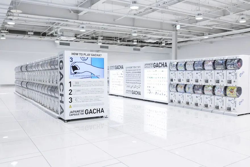 Minimalist rows of white capsule-toy vending machines in a bright, all-white airport-like space.