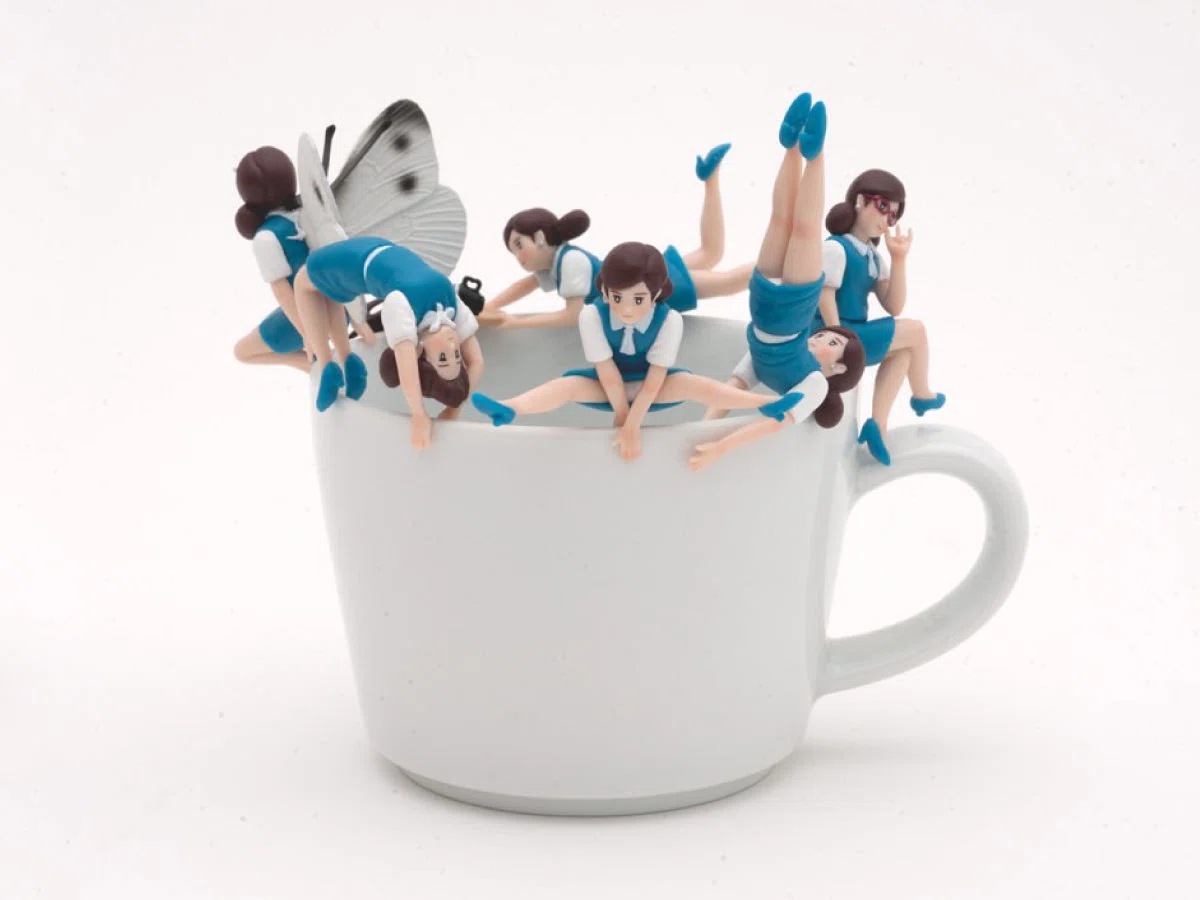 Several Fuchico on the Cup mini figures in blue uniforms posed around the rim of a white mug.