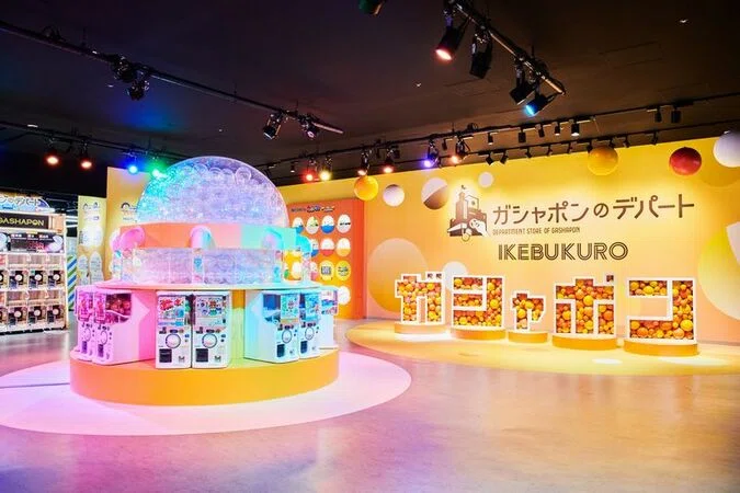 Ikebukuro Gashapon Department Store interior with a large capsule dome display surrounded by yellow walls and rows of gacha machines.