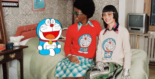 Two models sitting on a bed wearing Gucci knitwear with large Doraemon graphics, next to an animated Doraemon illustration.