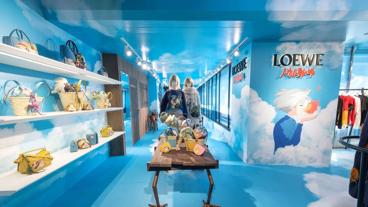 Interior of the LOEWE × Howl’s Moving Castle pop-up with sky‑blue walls, clouds, and shelves filled with bags featuring characters like Howl and Calcifer.